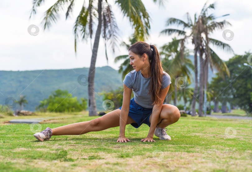 Скачать Молодая стройная женщина сидит на корточках и делает спортивные упражнения на фоне заката и пляжа с пальмами фотосток Ozero