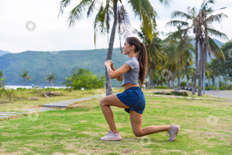Скачать Молодая стройная женщина сидит на корточках и делает спортивные упражнения на фоне заката и пляжа с пальмами фотосток Ozero