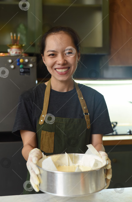 Скачать Вьетнамская женщина держит на кухне форму для выпечки с тестом для чизкейков фотосток Ozero