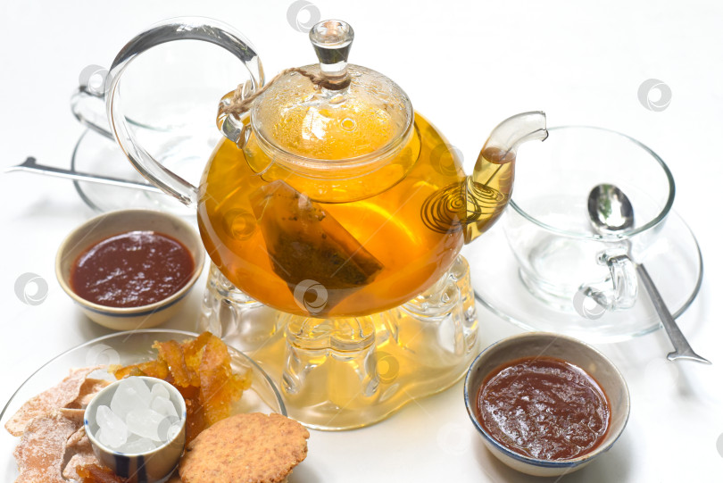 Скачать Стеклянный чайник с чашками, мармеладом и засахаренными фруктами на белом фоне фотосток Ozero