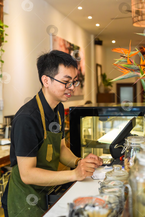 Скачать Вьетнамский официант, работающий за стойкой с кассовым аппаратом в кафе фотосток Ozero