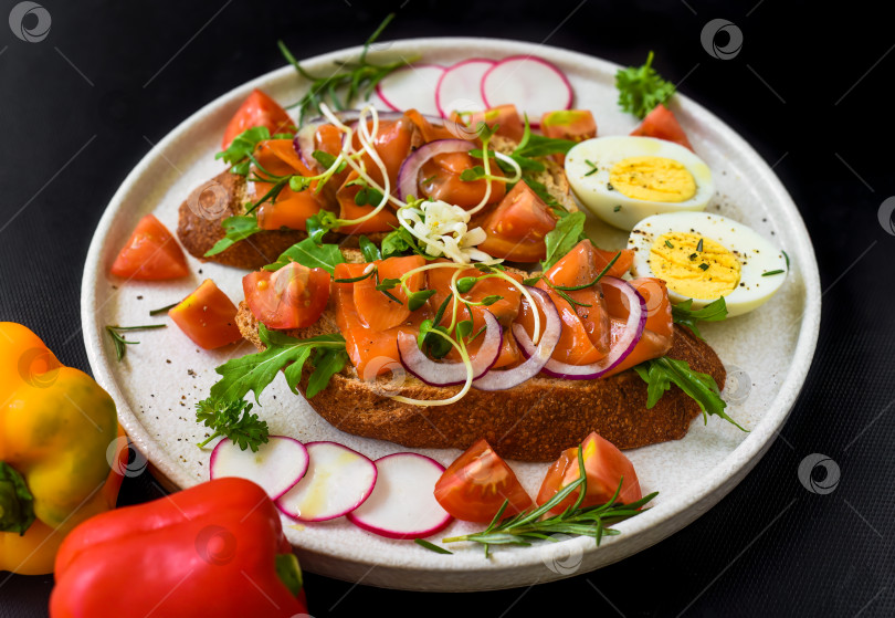 Скачать тосты с копченым лососем, луком и овощами на белой тарелке крупным планом фотосток Ozero