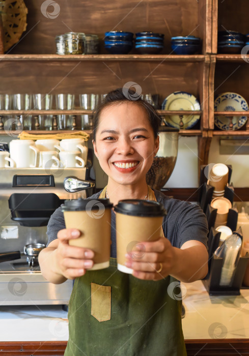 Скачать Улыбающаяся вьетнамская официантка держит бумажные стаканчики с кофе в кафе фотосток Ozero