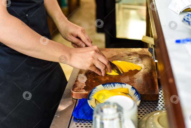 Скачать мужчина режет фрукт манго на деревянной доске в кафе фотосток Ozero