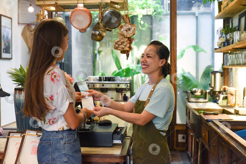 Скачать Молодая вьетнамская официантка работает с кассовым аппаратом и клиентами в кафе фотосток Ozero