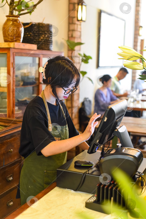 Скачать Молодая вьетнамская официантка обслуживает клиента на кассе в кафе. фотосток Ozero