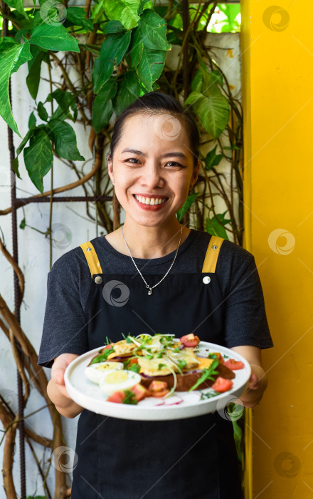 Скачать Молодая вьетнамская официантка держит в руках тарелку с куриными тостами фотосток Ozero