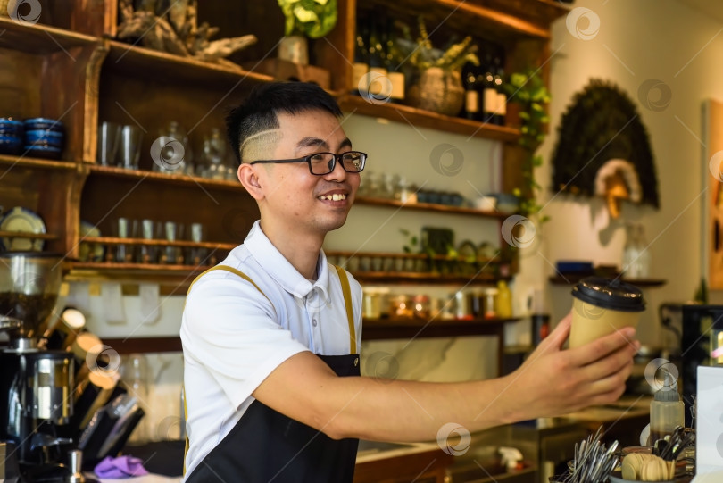 Скачать Улыбающийся вьетнамский официант держит бумажные стаканчики с кофе в кафе фотосток Ozero
