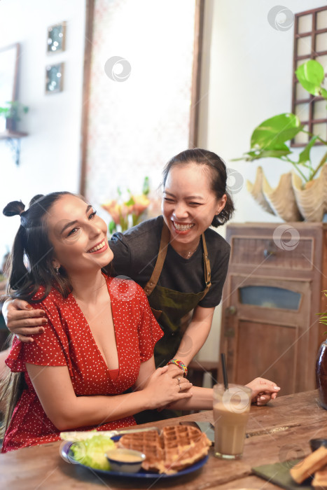 Скачать Молодая вьетнамская официантка улыбается и обнимает знакомого клиента фотосток Ozero