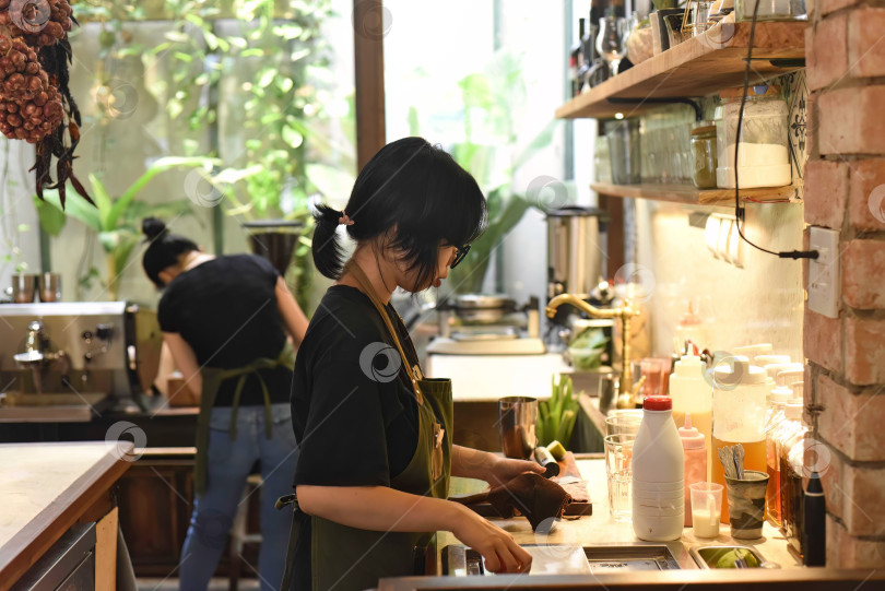 Скачать Вьетнамская официантка готовит заказ в кофейне фотосток Ozero