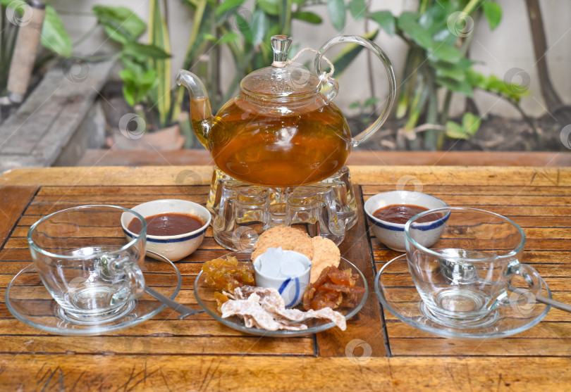 Скачать Стеклянный чайник с чашечками с мармеладом и засахаренными фруктами на деревянном столе фотосток Ozero