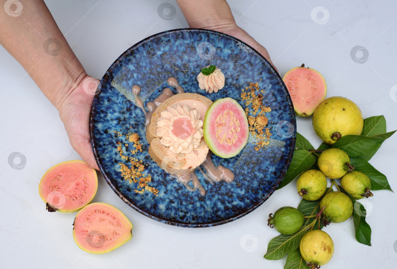 Скачать Рулет из гуавы на голубой тарелке на светлом фоне со спелыми плодами гуавы фотосток Ozero