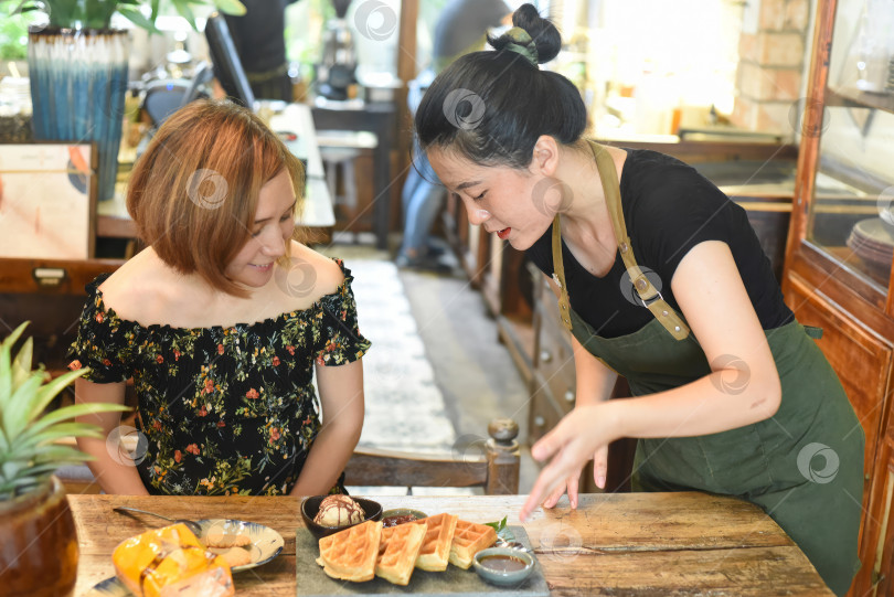 Скачать Вьетнамская официантка подала бельгийские вафли белой женщине фотосток Ozero