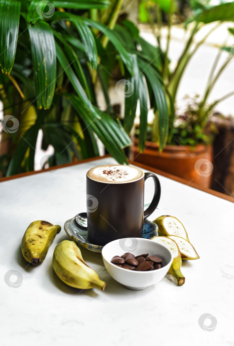 Скачать Бананово-шоколадный латте со свежим бананом и шоколадными каплями на белом столе фотосток Ozero