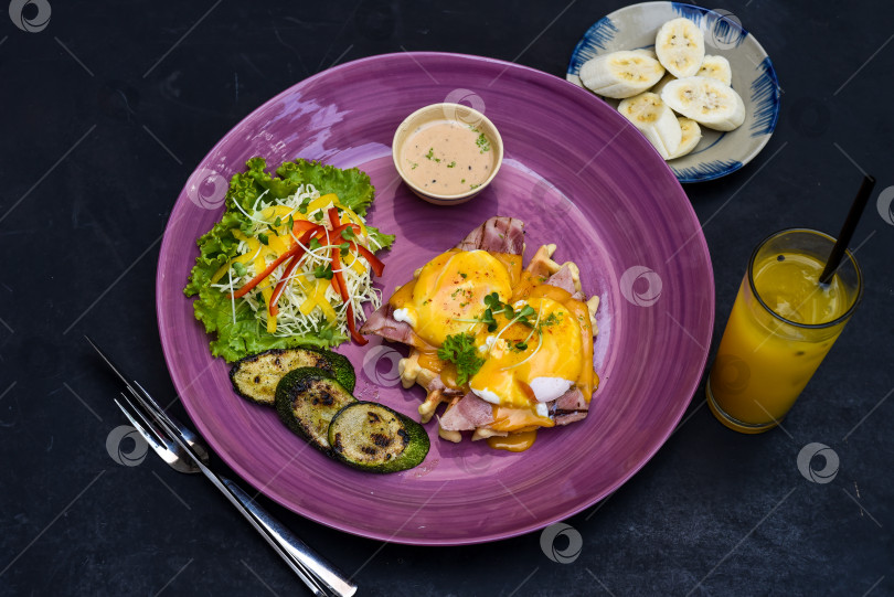 Скачать Яйца Бенедикт (яйца-пашот) на ветчине-гриль с голландским соусом, на бельгийских вафлях с цуккини-гриль, с тарелкой бананов и стаканом сока маракуйи фотосток Ozero