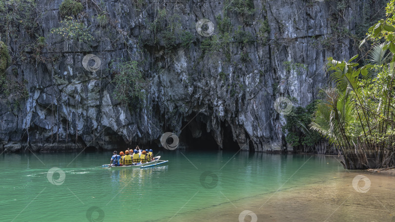 Скачать Лодка с туристами плывет по изумрудной реке ко входу в темную пещеру. фотосток Ozero