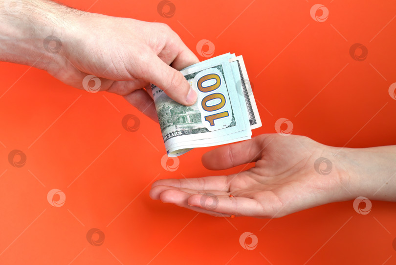 Скачать Рука, дающая сложенные деньги, доллар США в другой руке на красном фоне. Концепция взятки. фотосток Ozero