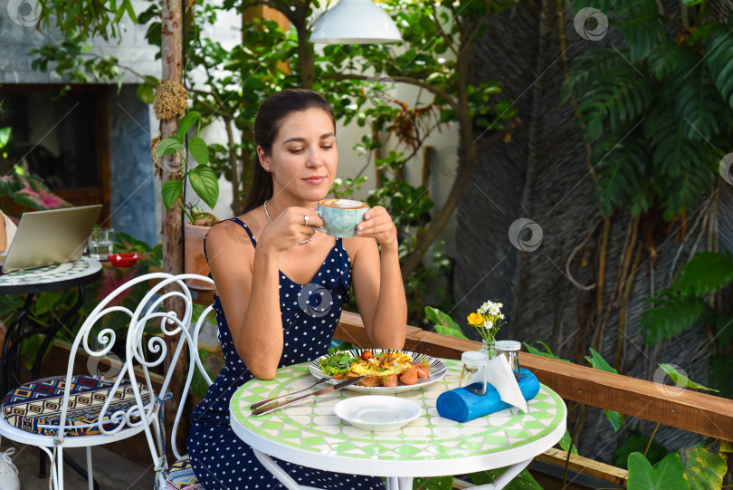 Скачать Счастливая русская 33-летняя женщина сидит в кафе, пьет капучино и счастливо улыбается, глядя по сторонам. фотосток Ozero