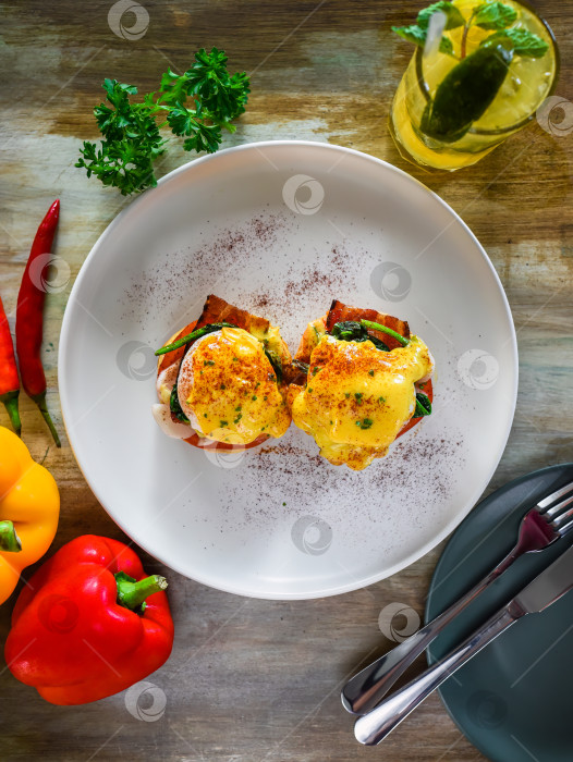 Скачать Английский маффин с яйцами-пашот, беконом и голландским соусом с овощами фотосток Ozero