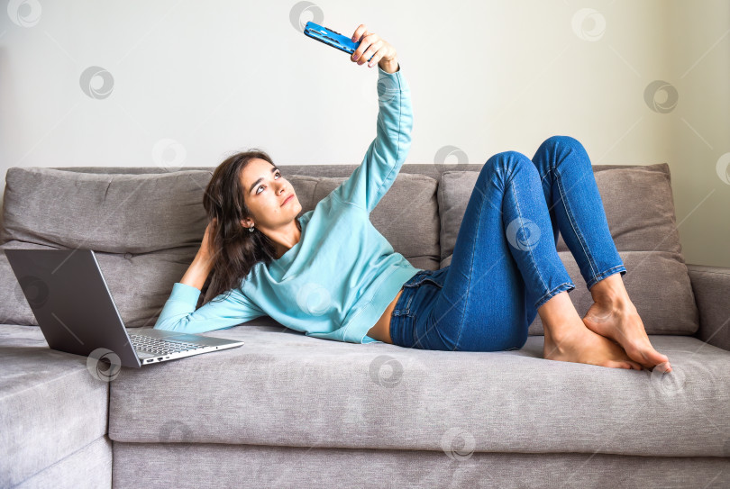 Скачать Молодая улыбающаяся женщина делает селфи для своего профиля. Она лежит дома на диване рядом с ноутбуком. карантин и концепция онлайн-знакомств фотосток Ozero