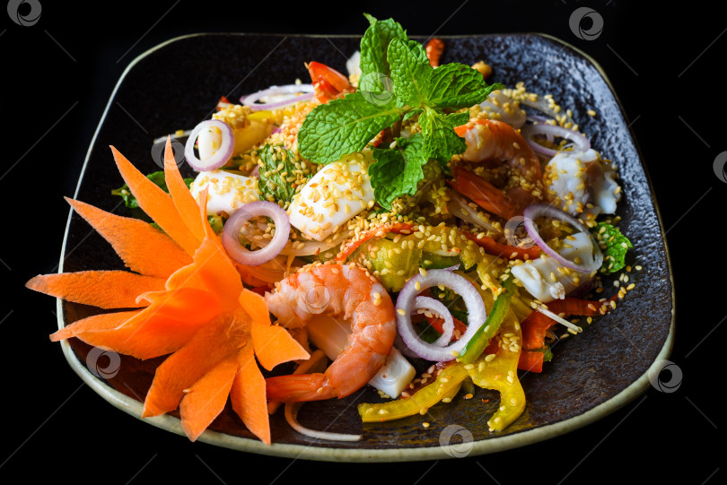 Скачать Тайский салат из креветок, кальмаров и лука, выделенный на черном фоне, вид сбоку фотосток Ozero
