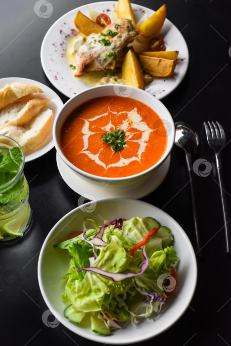 Скачать Обеденный набор из томатного крем-супа, салата, курицы с картофелем, лимонада на черном фоне фотосток Ozero