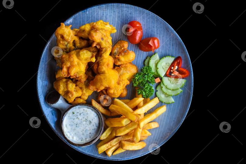 Скачать Жареная лягушка в кляре с картофелем фри на синей тарелке, выделенная на черном фоне, вид сбоку фотосток Ozero