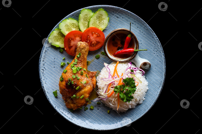 Скачать Запеченная куриная ножка по-вьетнамски с рисом, овощами и соусом на черном фоне, вид сверху фотосток Ozero