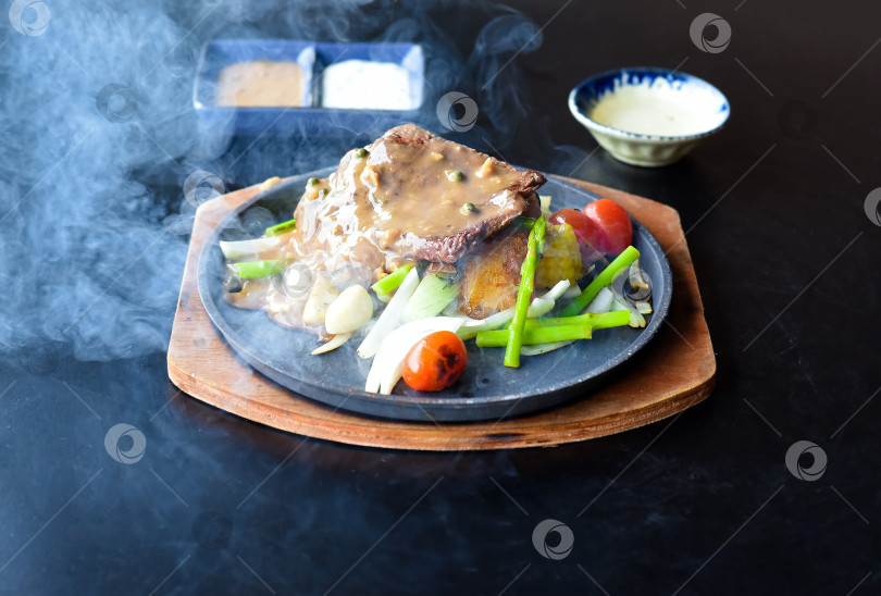 Скачать Запеченный на костре говяжий стейк с овощами и зеленью на тарелке, выделенный на черном фоне, вид сбоку фотосток Ozero