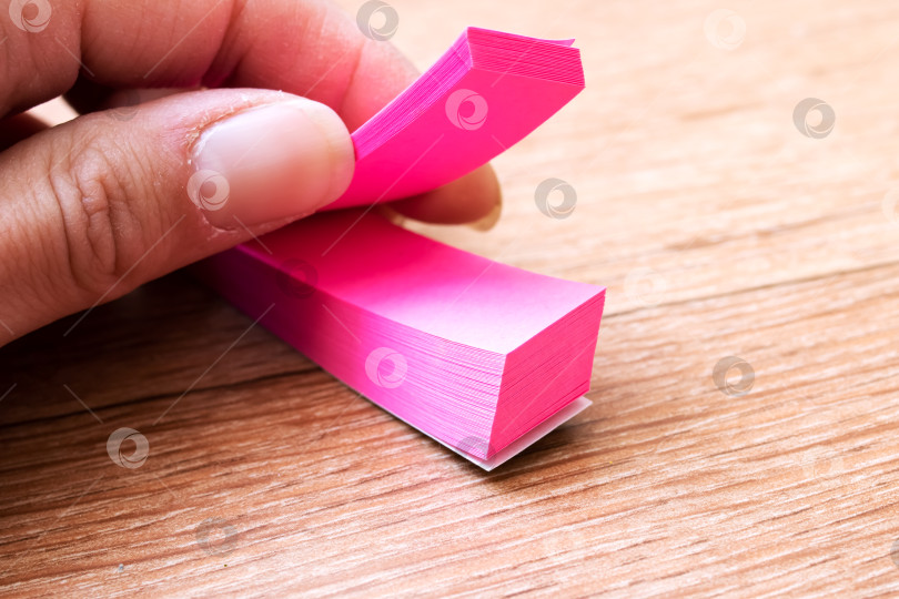 Скачать На деревянном столе кто-то держит пальцем розовую записку-стикер фотосток Ozero