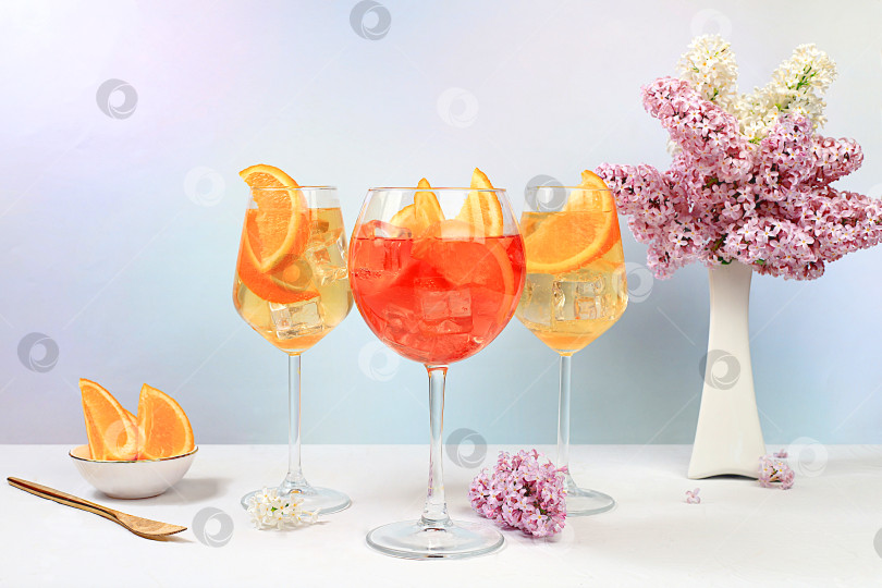 Скачать Праздничный алкогольный коктейль Aperol spritz в бокалах на ярком фоне с букетом сирени, концепция летнего бара, алкогольные напитки на вечеринке, реклама ресторанов и кафе, фотосток Ozero