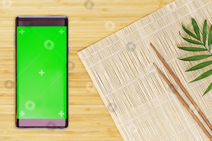 Скачать Природный коврик, деревянные палочки для еды и смартфон с зеленым экраном фотосток Ozero