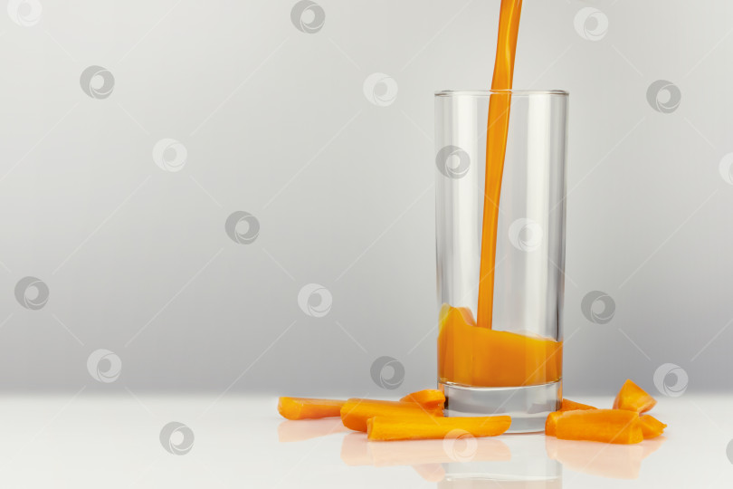 Скачать Морковный сок наливают в стакан, который стоит на белом столе фотосток Ozero