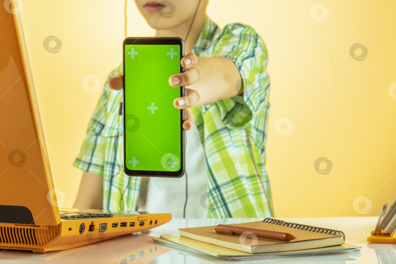 Скачать Мальчик в наушниках держит в руках телефон с зеленым экраном и совершает видеозвонок фотосток Ozero