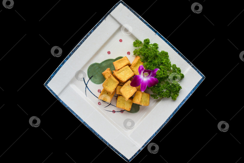 Скачать Вьетнамский жареный тофу на белой тарелке, выделенный на черном фоне для просмотра меню сверху фотосток Ozero