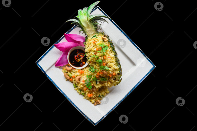 Скачать Жареный рис с морепродуктами в ананасе с овощами на синей тарелке, выделенный на черном фоне, вид сверху фотосток Ozero