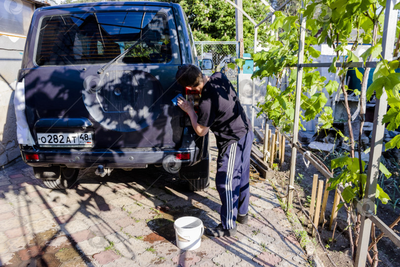 Скачать На снимке мужчина моет свою машину под высоким давлением воды на открытом воздухе. фотосток Ozero