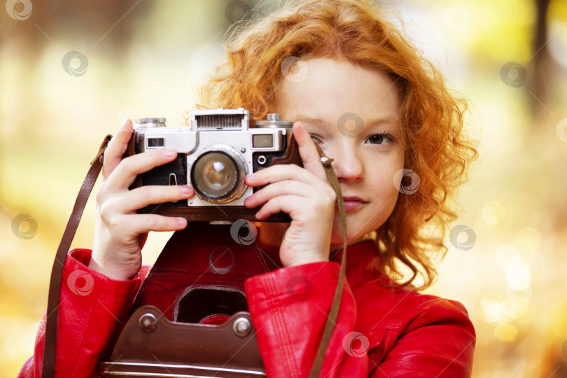 Скачать Маленькая рыжеволосая девочка с ретро-камерой на осеннем фоне. фотосток Ozero