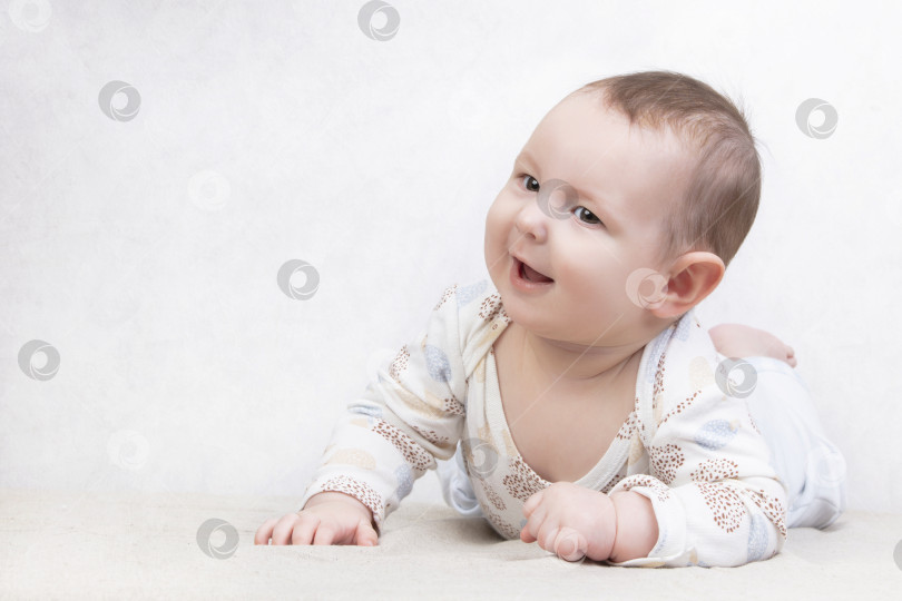 Скачать Малыш с улыбкой на белом фоне. Очаровательный шестимесячный мальчик лежит на кровати. Концептуальная фотография отцовства и материнства. фотосток Ozero