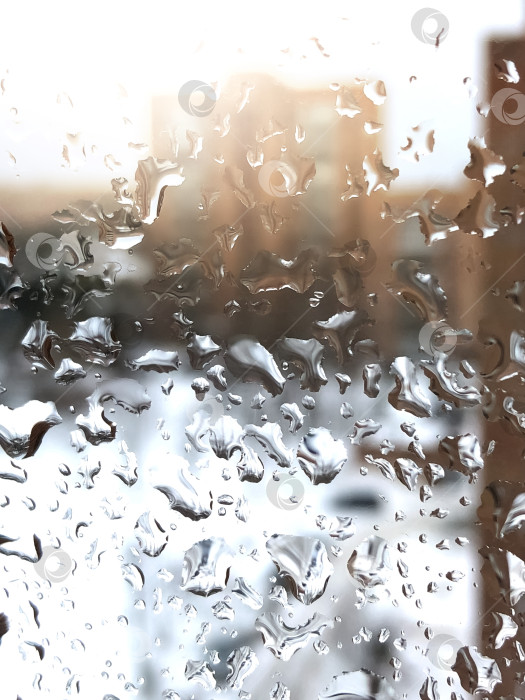 Скачать Капли дождя на оконном стекле с размытым изображением многоэтажного здания на заднем плане фотосток Ozero