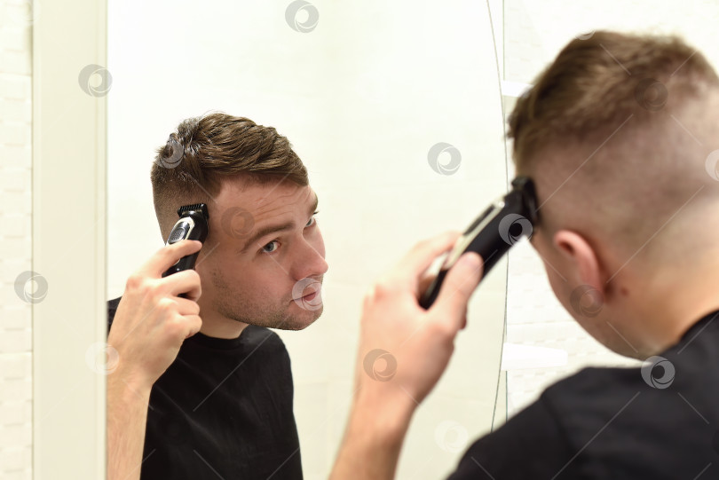 Скачать Молодой человек подстригает волосы и смотрится в зеркало в ванной комнате фотосток Ozero