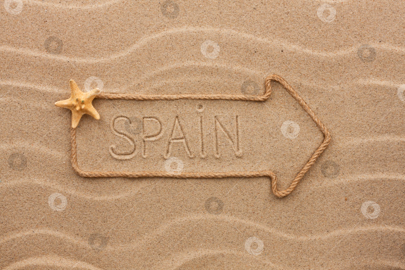 Скачать Стрела из веревки и морских раковин с надписью Spain на песке фотосток Ozero
