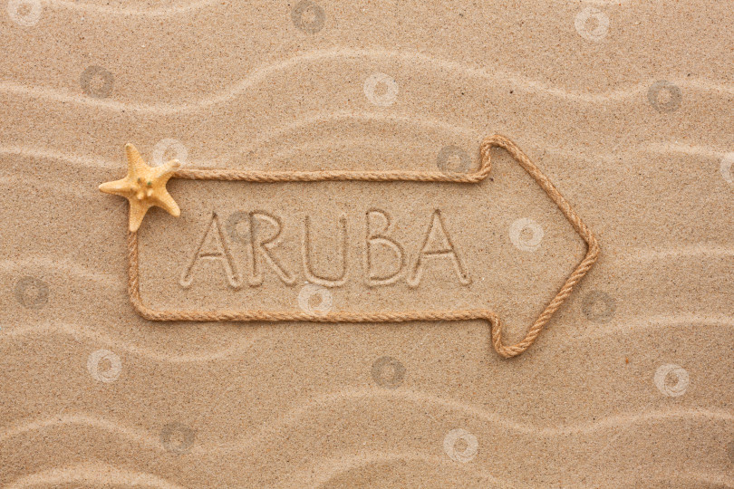 Скачать Стрела из веревки и морских раковин с надписью "Аруба" на песке фотосток Ozero