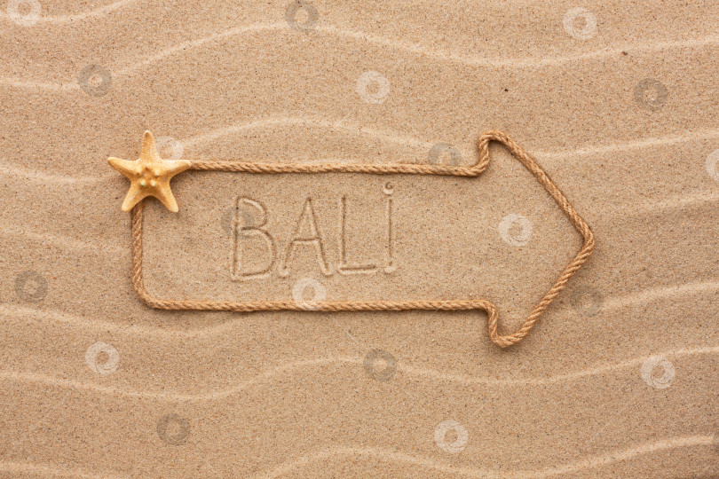 Скачать Стрела из веревки и морских раковин с надписью Bali на песке фотосток Ozero