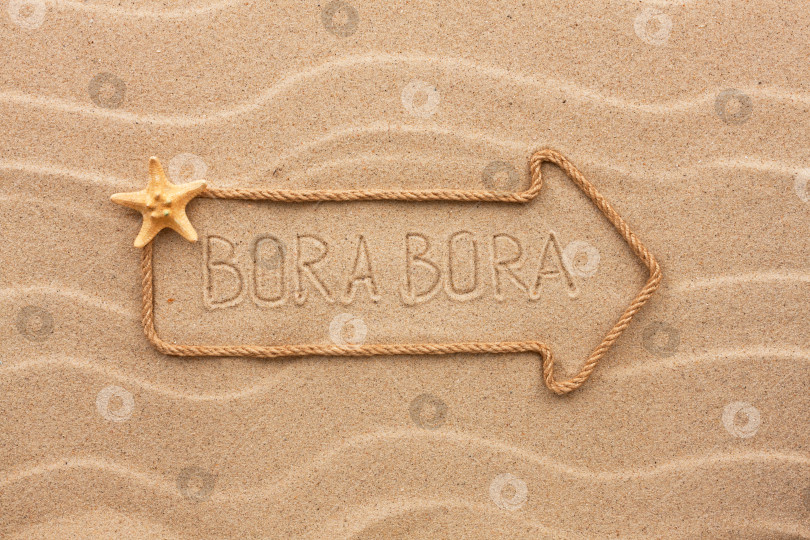 Скачать Стрела из веревки и морских раковин с надписью "Бора-Бора" на песке фотосток Ozero
