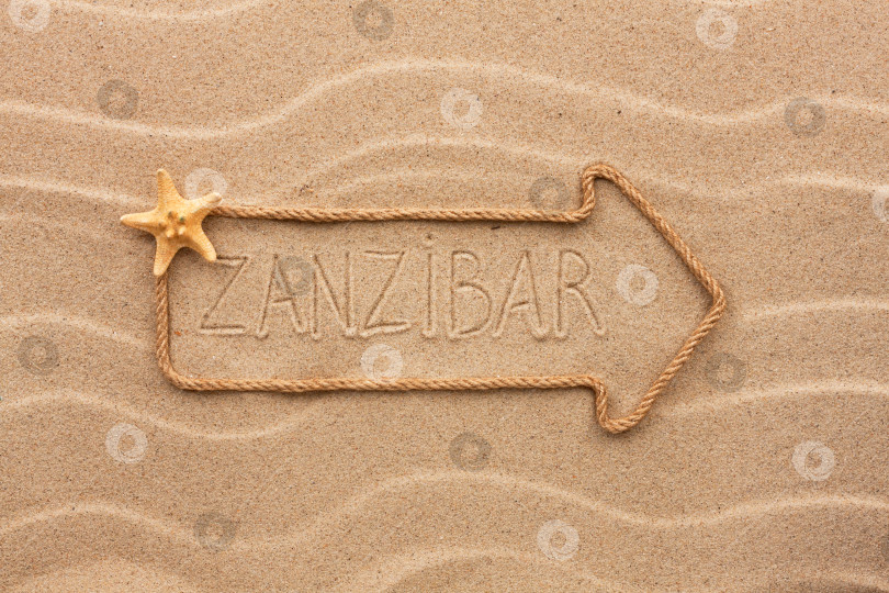 Скачать Стрела из веревки и морских раковин с надписью "Занзибар" на песке фотосток Ozero