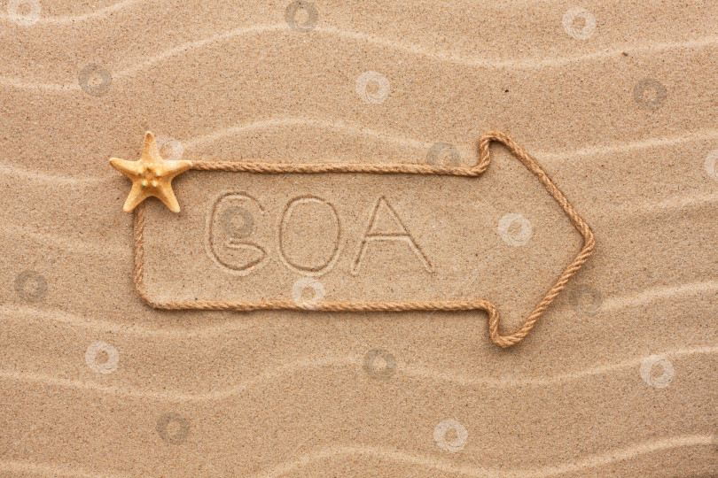 Скачать Стрела из веревки и морских раковин с надписью "Гоа" на песке фотосток Ozero