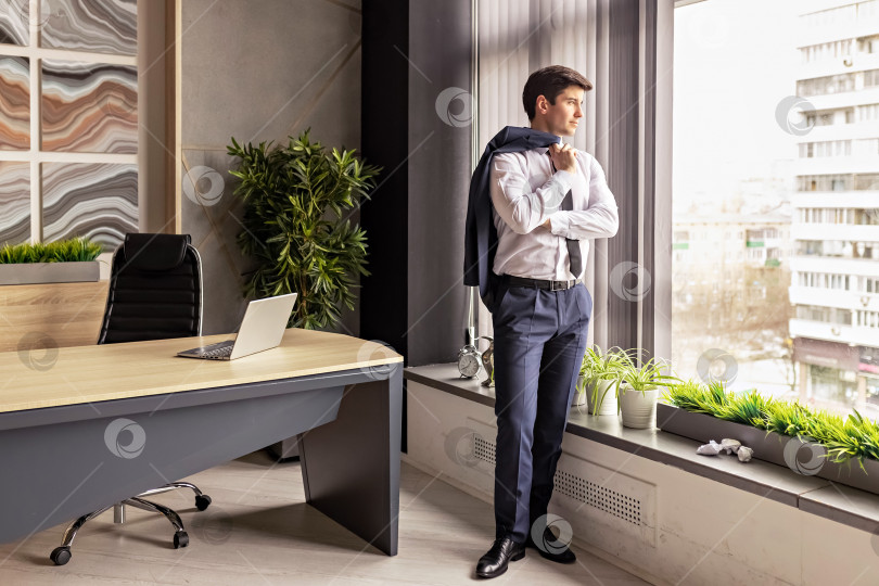 Скачать Большое окно с панорамным видом на молодого успешного бизнесмена в его собственном офисе, смотрящего вдаль, строящего планы или принимающего решение. Вдумчивый белый генеральный директор, размышляющий об успехе. фотосток Ozero