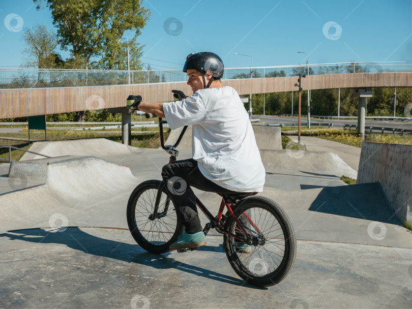 Скачать Молодой велогонщик BMX улыбается, позируя в скейтпарке фотосток Ozero