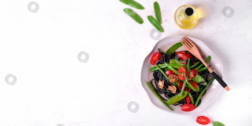 Скачать Веб-баннер с черными макаронами-спагетти, которые подаются с овощами: зеленым горошком, фасолью, перцем-гриль и грибами на тарелке на белом столе. фотосток Ozero